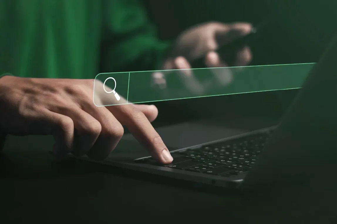 Main sur un ordinateur portable devant une barre de recherche lumineuse