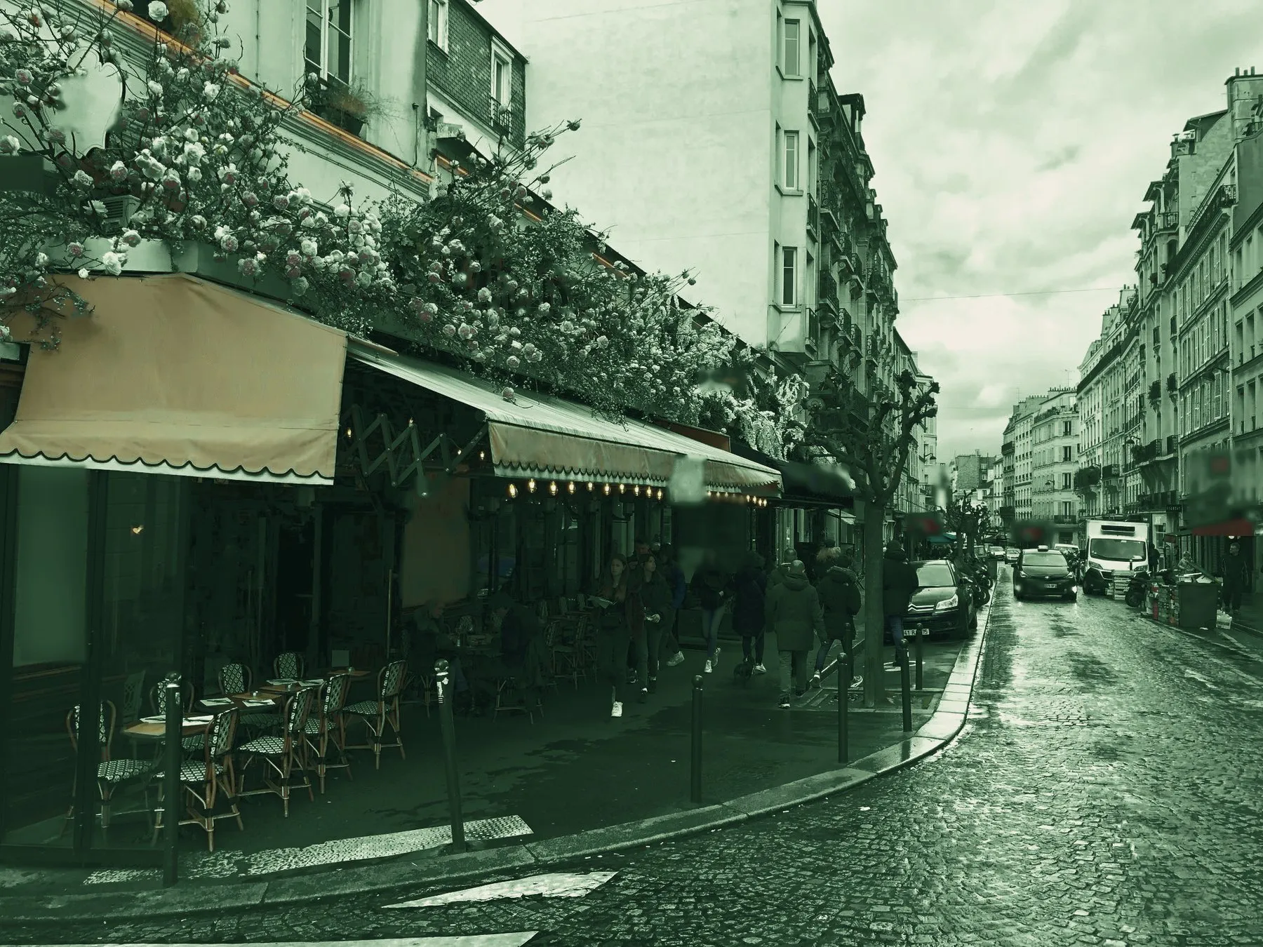 Terrasse de café parisien fleurie, rue pavée, en tons verts