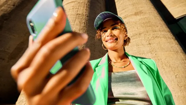 Jeune femme souriante en veste verte prenant un selfie au soleil