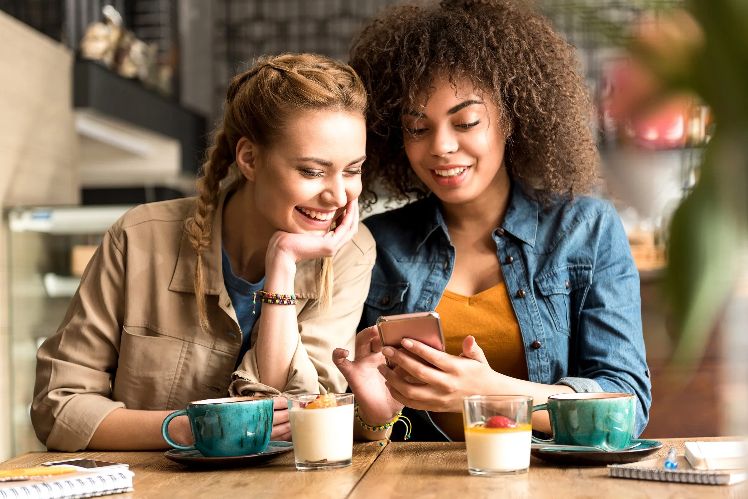 Deux amies au comptoir d’un coffee shop, cafés et téléphone en main