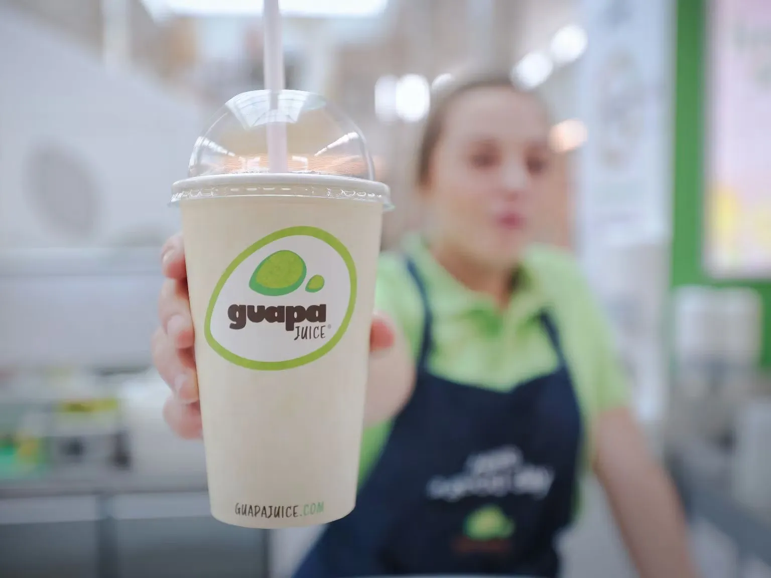 Une employée de Guapa Juice tend un gobelet de jus au logo de l’enseigne