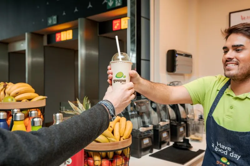 Un membre de l’équipe Guapa Juice tend un jus frais à un client par-dessus le comptoir.